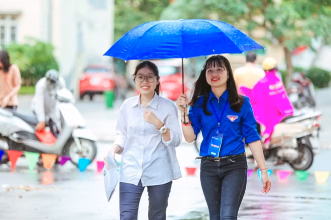 Buổi sáng của ngày thi thứ hai, tiết trời Hà Nội phần nào đó giảm nhiệt với cơn mưa nhỏ. Hình ảnh một bạn nữ tình nguyện viên với chiếc ô trên tay vội vã như con thoi liên tục đưa các thi sinh vào điểm thi tại trường THPT Nguyễn Tất Thành (Hà Nội).