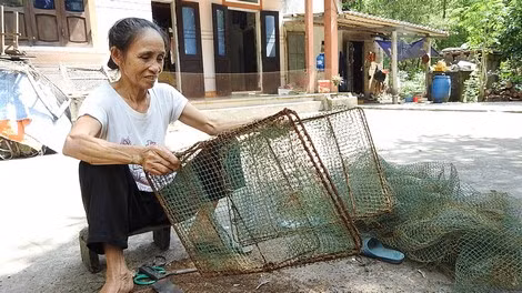 Bà Tình đang ngồi cắt bỏ lưới cũ rập cua để làm mới lại ngư cụ.