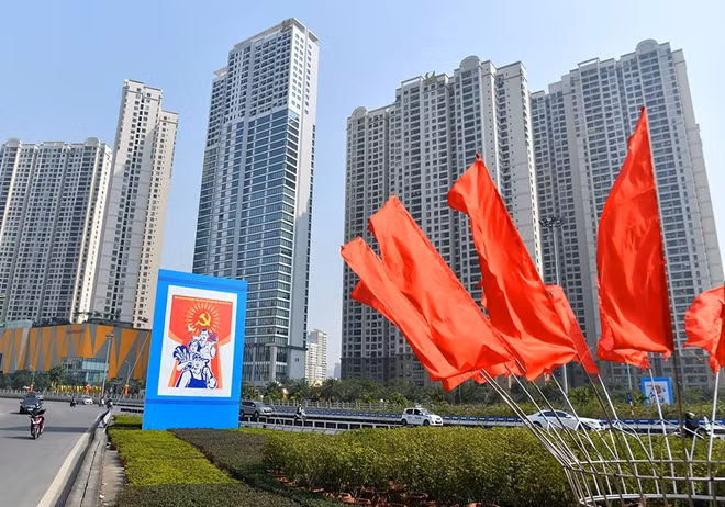 Nút giao Phạm Hùng - Trần Duy Hưng, đại lộ Thăng Long những ngày này rực rỡ cờ hoa. Một tấm panô hình khối ba mặt được trang hoàng bên dải phân cách nằm đối diện với Trung tâm Hội nghị quốc gia, nơi vài ngày tới sẽ diễn ra sự kiện chính trị trọng đại của đất nước - Đại hội đại biểu toàn quốc lần thứ XIII của Đảng diễn ra từ ngày 25/1 đến 2/2. Xung quanh đó là sắc màu đỏ rực của cờ Tổ quốc, cờ Đảng, panô, áp phích.