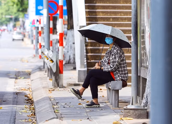 Một cô gái đi làm về với chiếc ô trên tay để che nắng trong lúc chờ xe buýt.