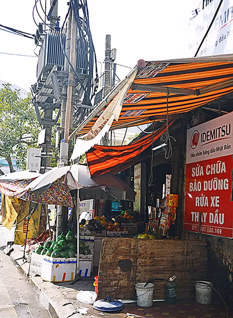 Một quán bán hoa quả và cửa hàng sửa xe máy nằm sát trạm biến áp trên phố Thụy Khuê