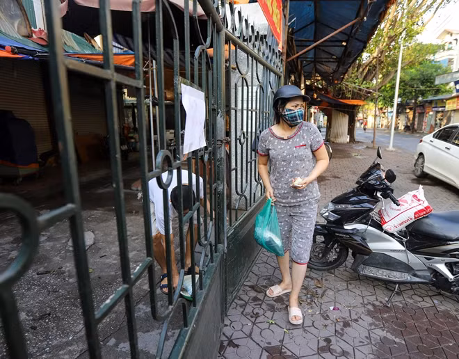 Người dân đi mua đồ nhận hàng qua cánh cửa sắt khóa chặt.