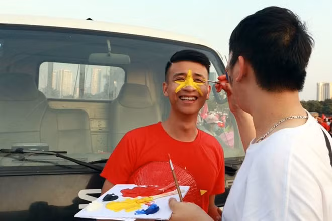 Một CĐV tranh thủ "trang điểm" cờ đỏ sao vàng trước khi vào sân cổ vũ.