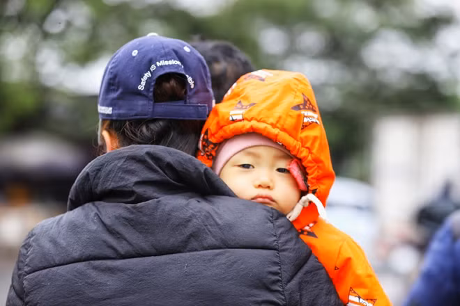 Em bé với áo ấm trùm kín người cùng bố mẹ đi trên phố trong ngày mưa rét.