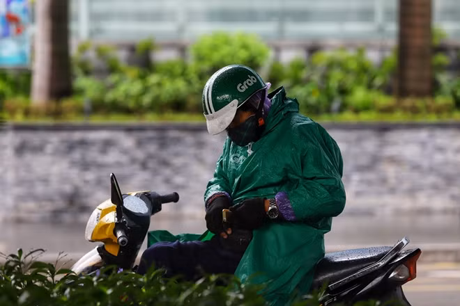Một tài xế xe ôm công nghệ trùm áo ấm cùng áo mưa để chống lại cái lạnh cùng mưa rét chuẩn bị cho đón khách.