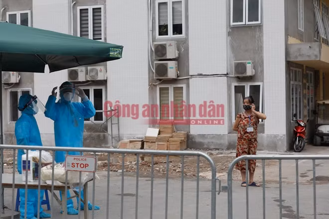 Người phụ nữ giữ khoảng cách với hàng rào cách ly và gọi điện cho người thân chờ tiếp tế đồ dùng.