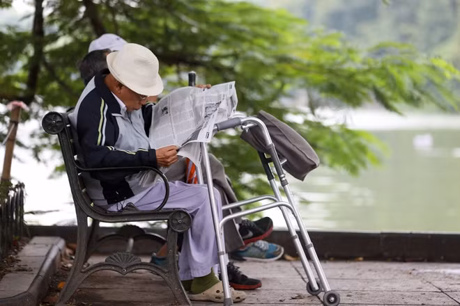 Cụ ông với chiếc áo khoác giữ ấm cơ thể, thanh thơi ngồi đọc báo bên bờ hồ Gươm trong không khí se lạnh của đợt gió mùa đông bắc.