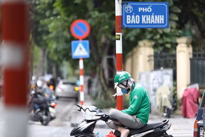 Một anh chàng xe ôm công nghệ co ro ngồi chờ khách trên đường.
