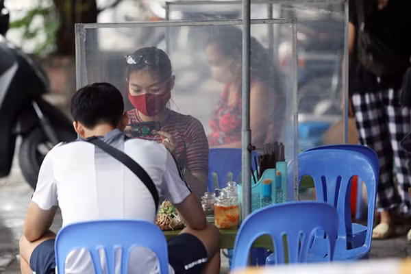 Hai thực khách ngồi đối diện nhau nhưng được ngăn cách bởi một tấm chắn từ chất liệu nilon dựng lên ở giữa. Hình ảnh được ghi lại tại một quán ăn trên phố Lê Duẩn (Hà Nội).