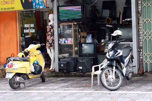 Một cửa hàng sửa chữa đồ điện tử trên phố Ngọc Hà, chiếc tivi đã được mở sẵn bóng đá nhưng khán giả chỉ có 1 chiếc ghế nhựa cùng hai chiếc xe máy.