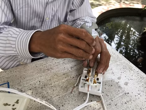 Hai tay anh Minh thoăn thoắt tháo ốc vít, tước vỏ nhựa dây điện trước khi lắp hoàn chỉnh bộ ổ cắm.