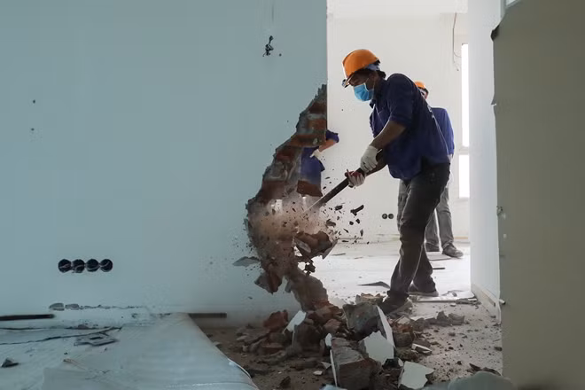 Công nhân dùng búa tạ phá dỡ tường ngăn trong một căn hộ.