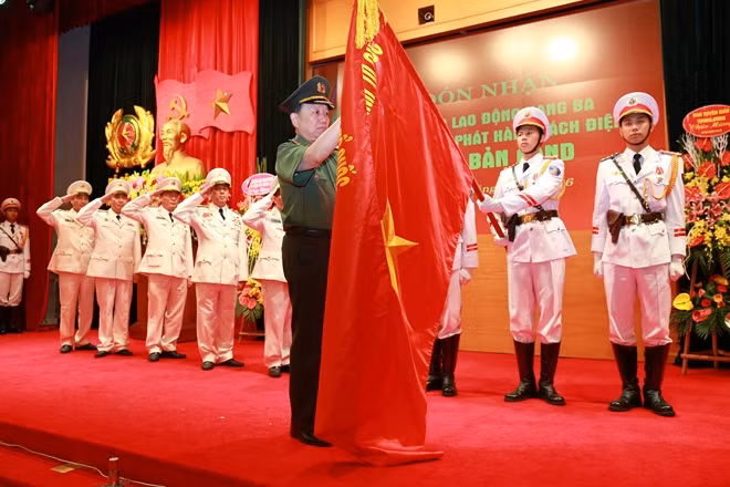 Thừa ủy quyền của Chủ tịch nước, Bộ trưởng Tô Lâm gắn Huân chương Lao động hạng Ba lên lá cờ truyền thống của NXB CAND.
