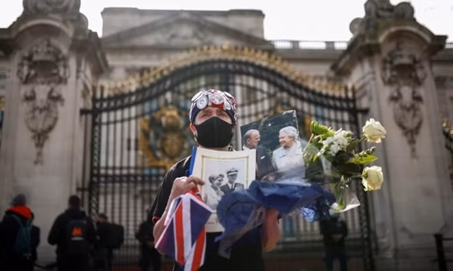 Một người đàn ông cầm hoa và ảnh của vợ chồng Nữ hoàng Anh bên ngoài Cung điện Buckingham, London, hôm 9/4. Ảnh: Reuters.