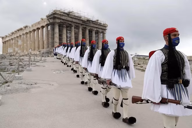 Các thành viên đội cận vệ của tổng thống Hy Lạp hành quân trước đền Parthenon, đỉnh đồi Acropolis, sau lễ hạ cờ kỷ niệm hai trăm năm ngày bắt đầu cuộc chiến giành độc lập chống lại đế chế Ottoman. Ảnh: Petros Giannakouris/AP.