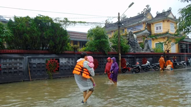 Một du khách nước ngoài bồng bế con nhỏ đi lánh vùng thấp lũ ở Hội An.