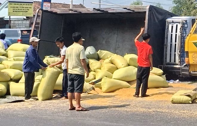 Hiện trường xe ô tô tải lật nghiêng, hàng chục bao lúa đổ xuống mặt đường.