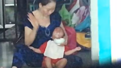 Bảo mẫu áo xanh dùng tay đánh vào mặt cháu bé khi cho ăn (Hình cắt từ clip)