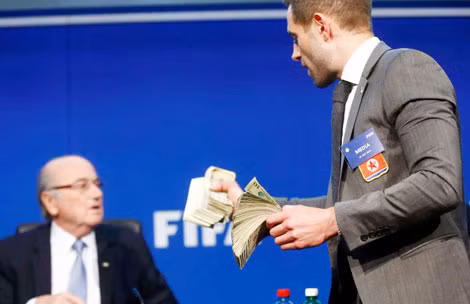 Brodkin cầm hai cục tiền 10 USD giả tiến tới Blatter.