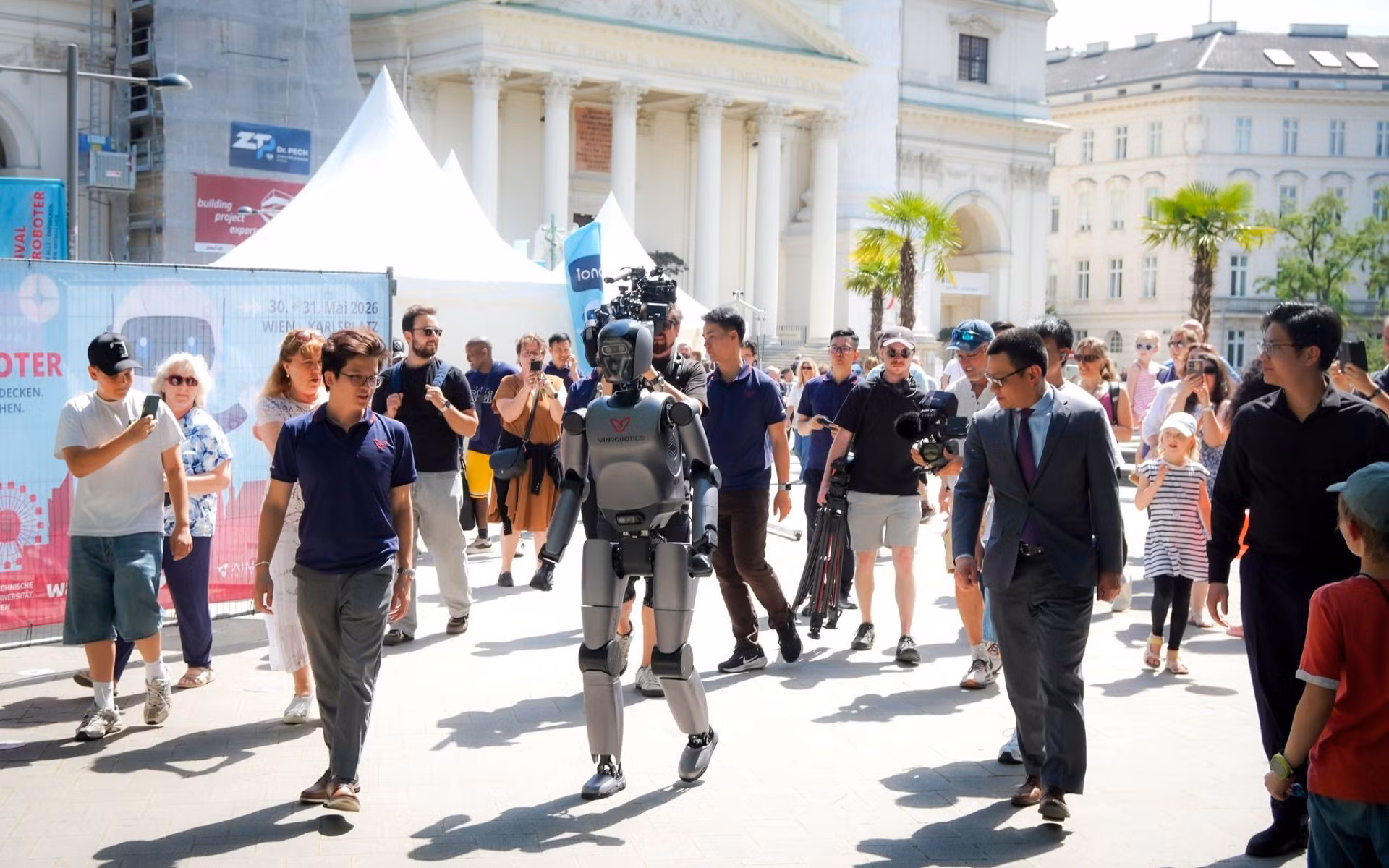 VR-H3 của VinRobotics thu hút sự chú ý với khả năng di chuyển tự nhiên tại Festival der Roboter 2026, dưới sự chứng kiến của Đại sứ Việt Nam tại Áo, ông Vũ Lê Thái Hoàng (thứ hai từ phải sang trái, hàng trên), cùng đông đảo khách tham quan quốc tế. Nguồn: VinRobotics